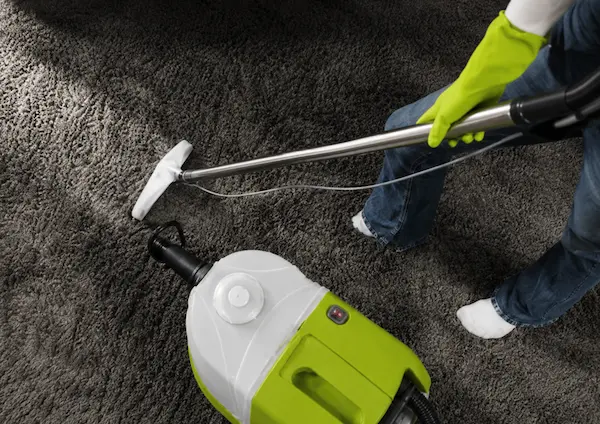 Overhead view of carpet cleaning technician using steam extraction wand on a grey carpet